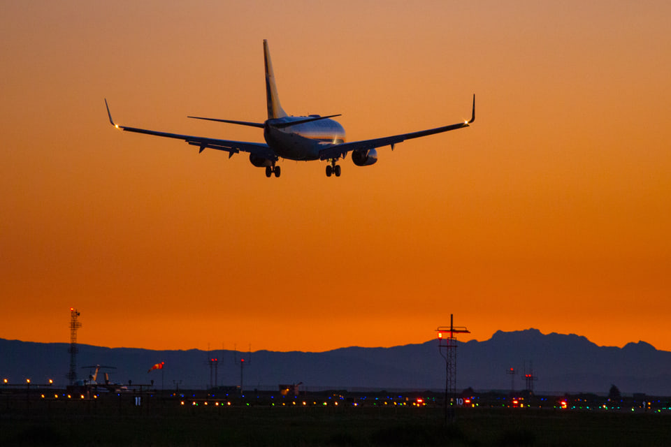 Passenger aircraft descending toward an airport against an orange sunset sky.