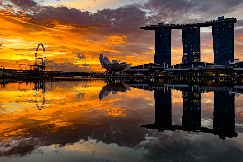 Marina Bay skyline reflected in water beneath an orange sunset.